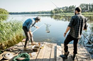 two men on vacation standing on a dock fishing on a lake