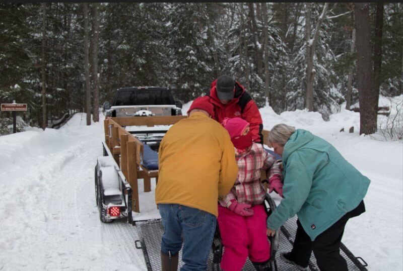 wheelchair-bound person getting help on a wagon to sit-ski
