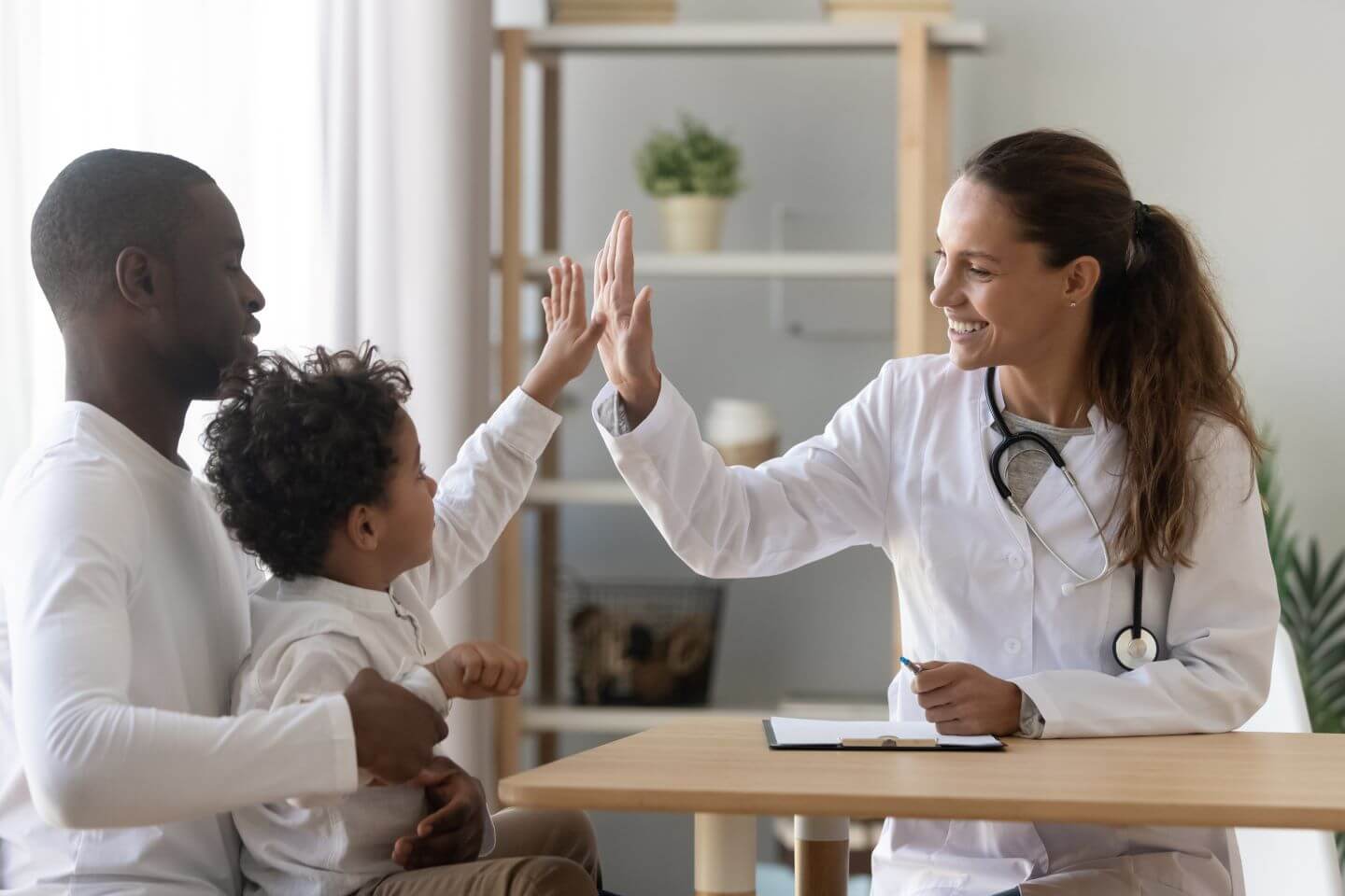 nurse practitioner NP high fiving a young male patient sitting with his father