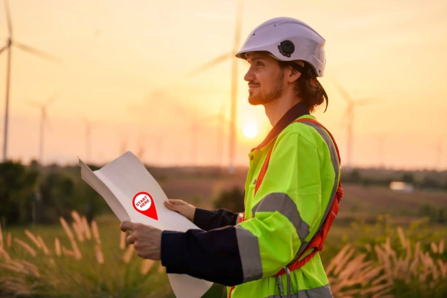 A civil engineer in a field as the sun sets in the background with windmills