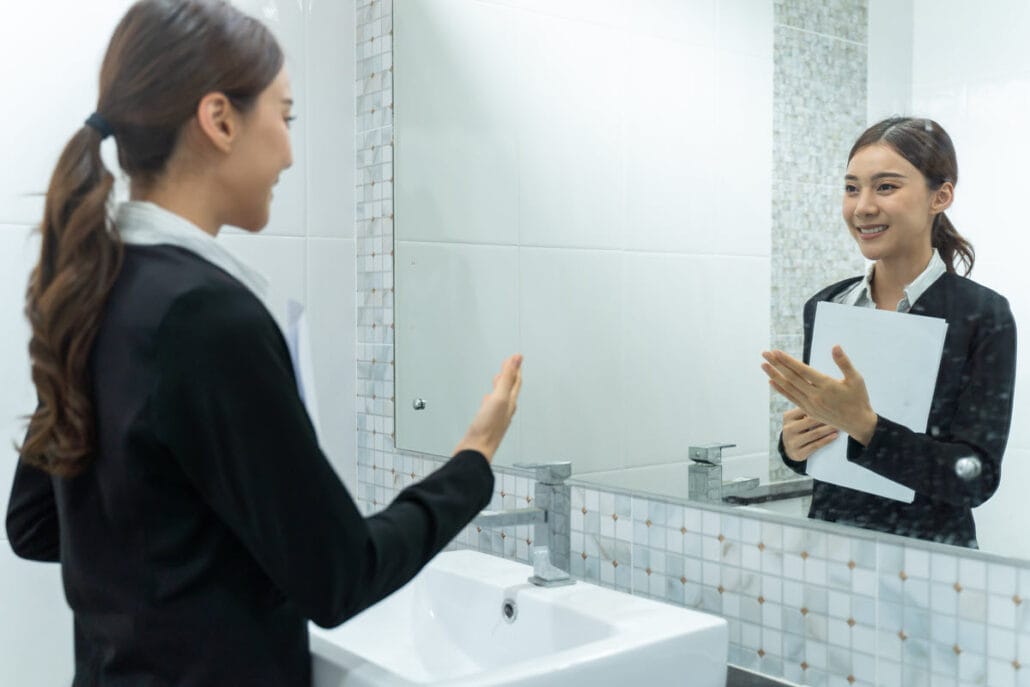 Woman preparing to present herself at a networking event by practicing in front of a mirror