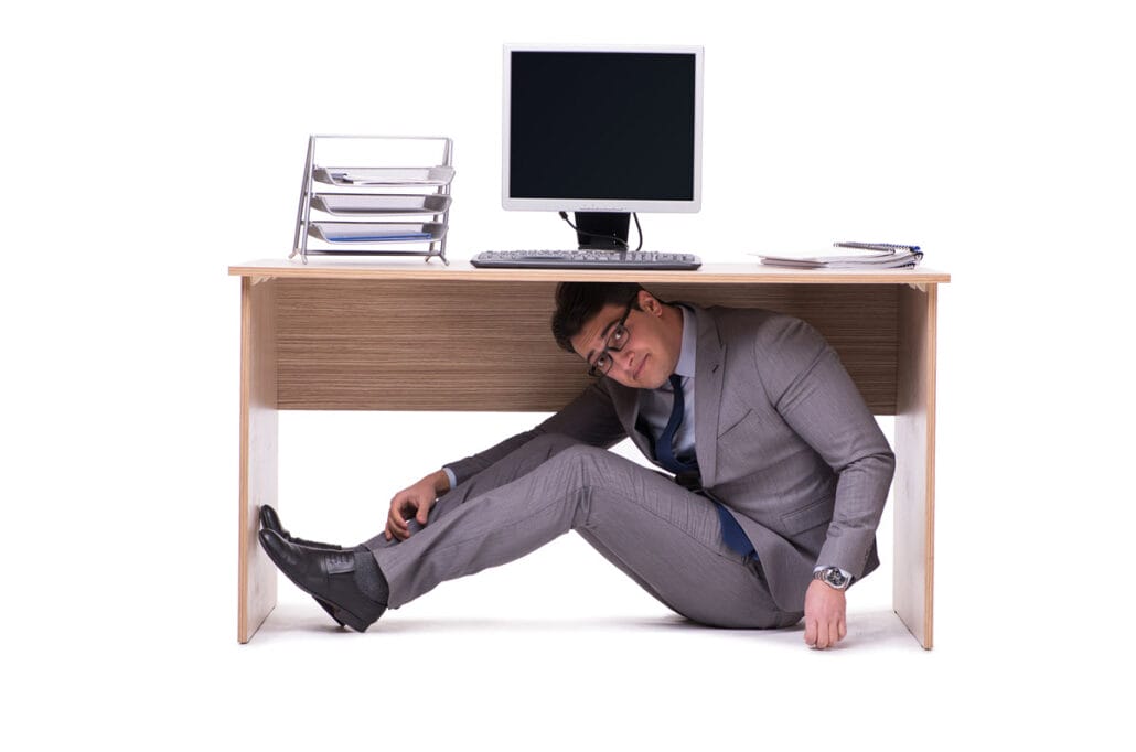 A man hiding under his desk depicting the impact of difficult coworkers on the job.