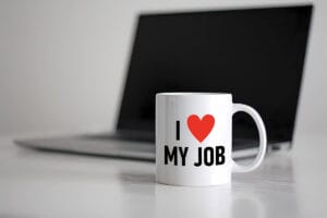 A laptop on a table with a coffee mug in front of it that says I Love My Job