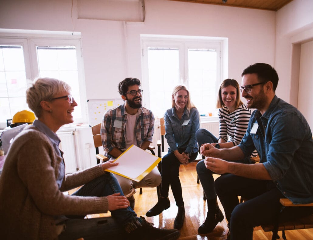 Workers sitting in a circle smiling and talking, representing a positive work environment.