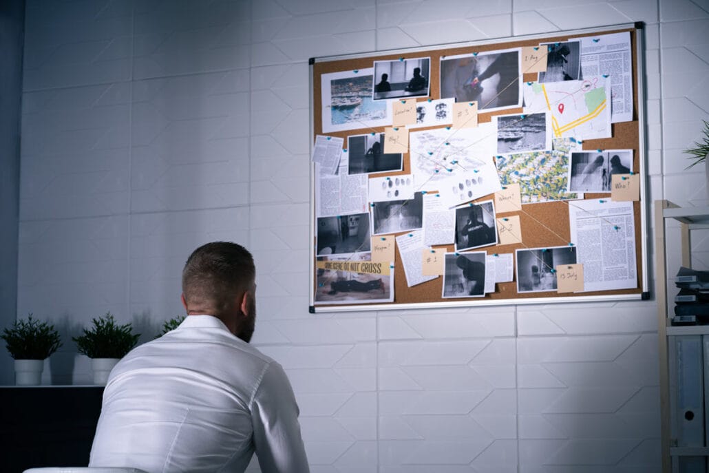 A private investigator looking at photos on a bulletin board in his home