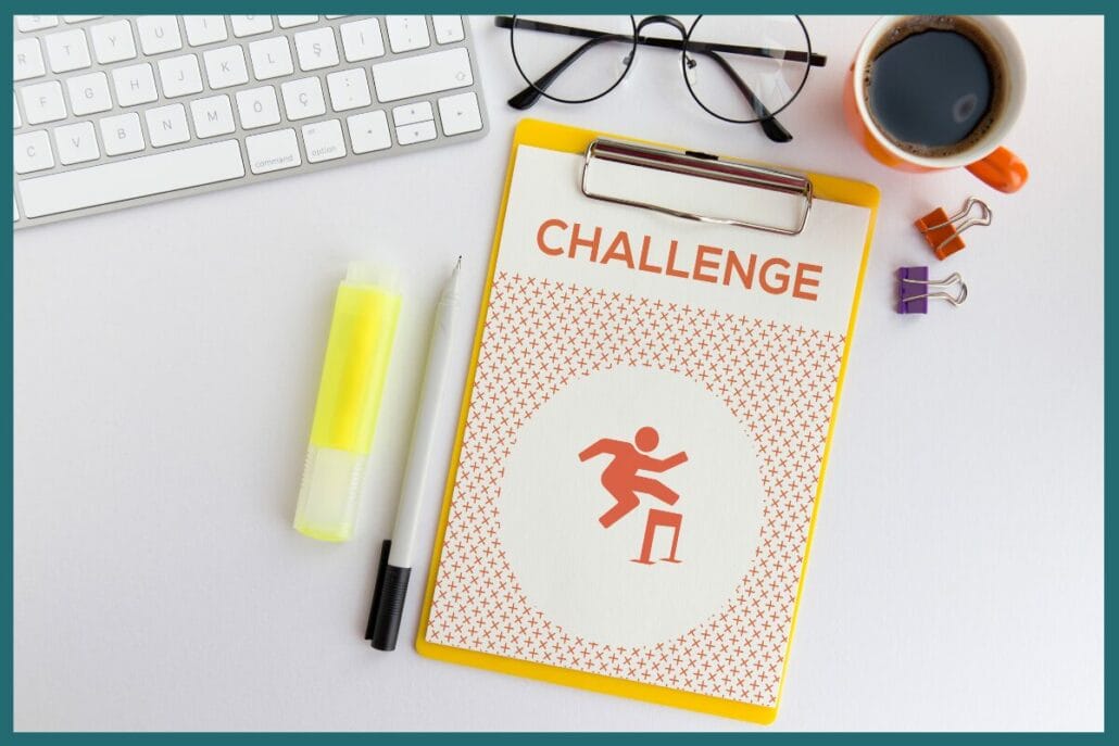 An overhead view of a desk with a clipboard showing a paper that says challenge with a person jumping over a hurdle