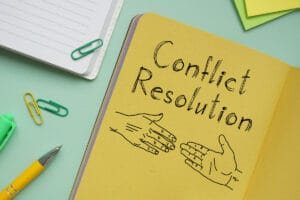 A close-up of a yellow notebook with the words "Conflict Resolution" written on it, with a drawing of two hands shaking