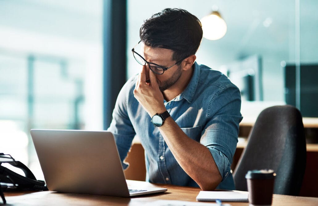 An illustration showing the concept of job burnout with a man at his laptop with a look of stress