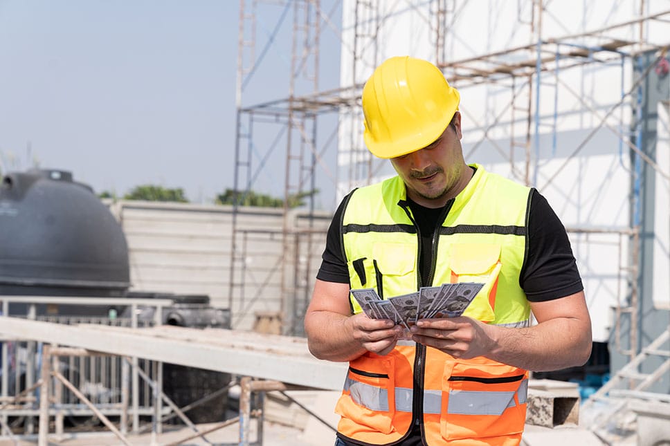 worker wearing hard-hat counting their salary from their engineering occupation at a construction site