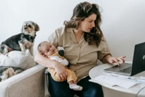 Mother holing infant, browsing on laptop for returning to work after maternity leave